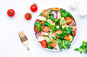 Salad with chicken slice, tomatoes, cucumber, onion, lettuce and sesame seeds on white background, top view