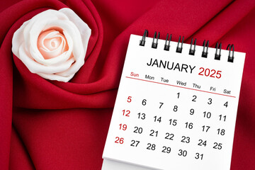 January 2025 desk calendar and pink rose on red textile.