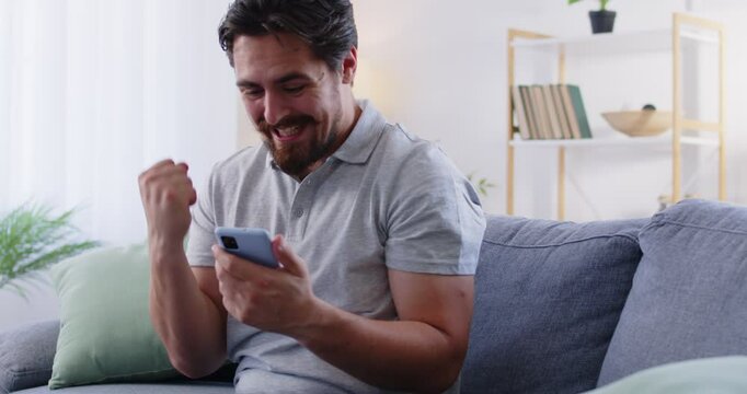 Happy cheerful lucky man uses online betting app on mobile phone, watches digital broadcast of horse race, football match or other sports event results, wins money, and receives sms text notification