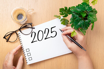 New year resolutions 2025 on desk. 2025 goals - hands and notebook, coffee cup, plant on wooden table. Resolutions, plan, goals, action,  idea concept. New Year 2025 resolutions, copy space