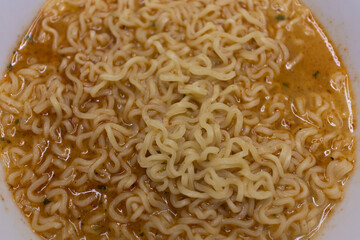 Yellow spicy noodles served in a white bowl, a flavorful and easy-to-make meal for noodle lovers .