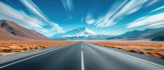 Low angle and wide shot of highway asphalt road with motion blur effect towards the horizon with blue sky and mountains in the background