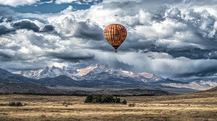 Obraz premium A single balloon rising into a cloudy sky, with a scenic mountain range in the background. No people.