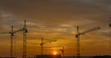 Footage of construction crane silhouette at sunrise time lapse. Silhouette of construction site building with the cranes on a orange sunrise time lapse footage. 4K DCI