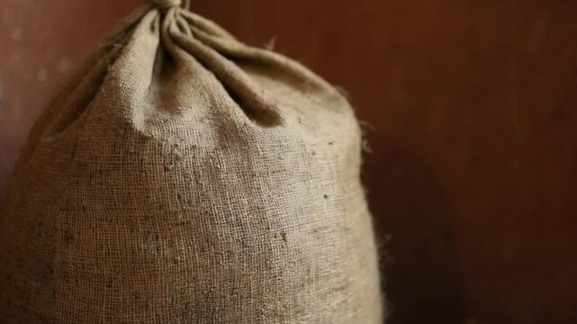 Aged sack of coffee beans against a rustic brown wall backdrop.