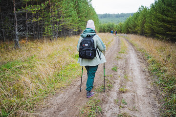 A woman is carrying a backpack and using walking poles as she makes her way down a dirt road that...