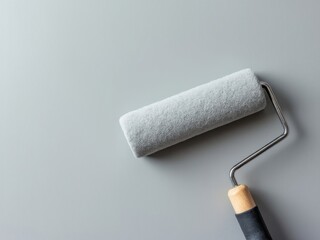Obraz premium Minimalist composition of a paint roller with a wooden handle on a smooth gray background, representing painting tools and home renovation
