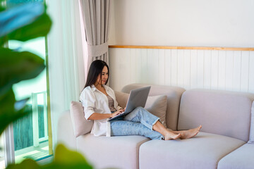 Young Asian female relaxing and using laptop on a sofa at home