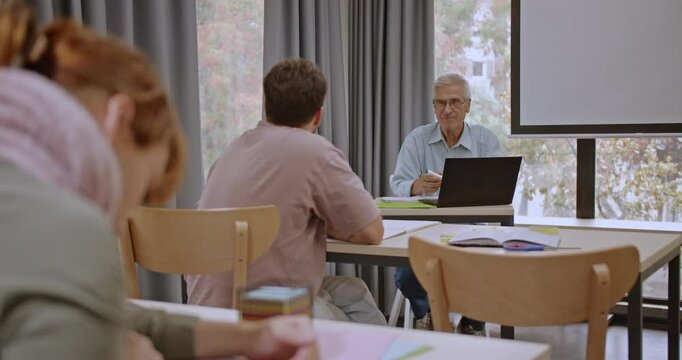 College students sit in a classroom, focused on their exam, while their professor observes attentively, ensuring a calm and orderly testing environment.