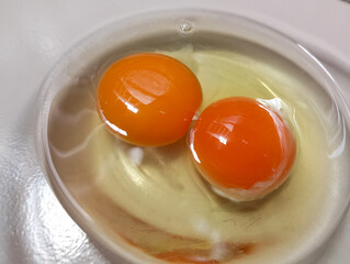 two fresh eggs with vibrant orange yolks in a glass bowl
