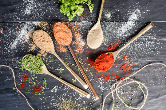 Spices sprinkled around on table with spoons