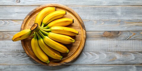Vibrant yellow bananas arranged on a rustic wooden plate, showcasing healthy tropical food. Ideal for stock photography, emphasizing freshness and