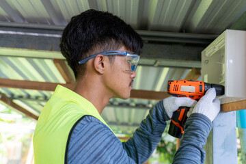 Male electrician installing electrical breaker box with cordless drill.