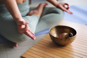 Woman in lotus position practicing yoga singing meditation bowl on wooden board top view closeup