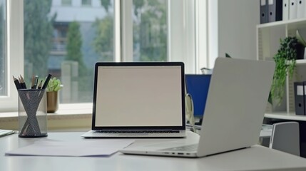 Front view laptop on white table. There is paper and a pen holder nearby. In modern office space