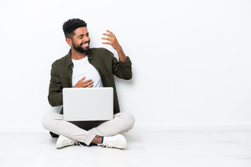 Young Brazilian man with a laptop sitting on the floor isolated on white making guitar gesture