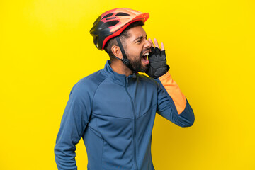 Young cyclist Brazilian man isolated on yellow background shouting with mouth wide open to the side