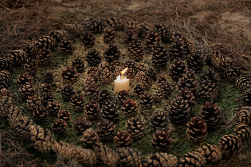 burning candle and nature mandala composed of pine cones on earth, dark natural background. mandala pattern of fallen cones in forest. magic, witchcraft, esoteric ritual with candle