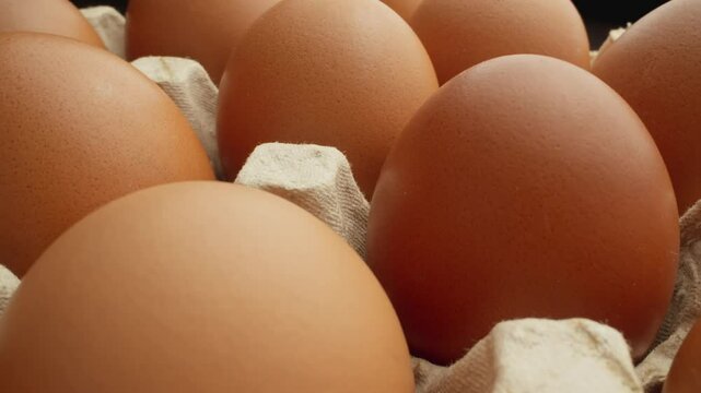 Brown eggs in carton, showcasing smooth texture and rich color against contrasting dark background. Dolly slider shot. Raw chicken eggs for sale at market. Close-up of hen eggs. Organic food. 4K, UHD