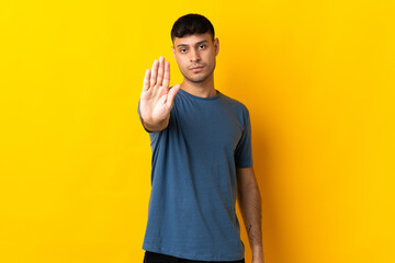Young Colombian man isolated on yellow background making stop gesture