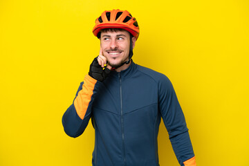 Young cyclist caucasian man isolated on yellow background thinking an idea while looking up