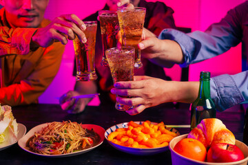 Three men are sitting at a table, holding glasses of beer and clinking glasses in celebration.They are enjoying food and drinks,eating and having fun in a party room with a happy,cheerful atmosphere