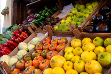 A variety of fruits and vegetables are displayed in wooden crates. The produce includes tomatoes, oranges, lemons, and peppers. Concept of abundance and freshness, as the colorful fruits