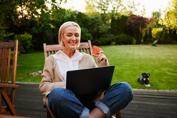 Mature woman enjoying afternoon in backyard using laptop eating watermelon