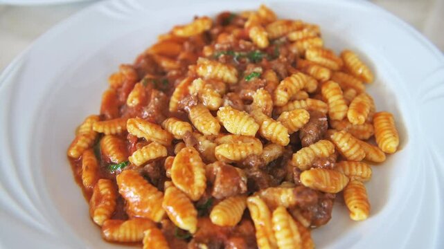 Malloreddos ala ragu della casa traditional sardinian mini dumplings pasta, tomato sauce, beef pork meat cheese on white plate, Sardinia macro closeup