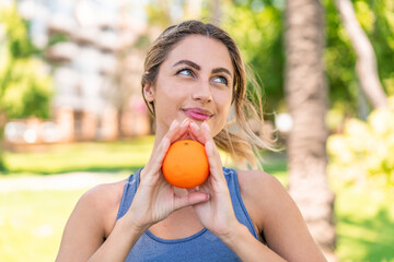 Young blonde woman at outdoors holding an orange