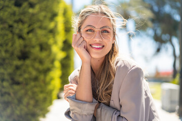 Pretty blonde Uruguayan woman with glasses at outdoors With happy expression