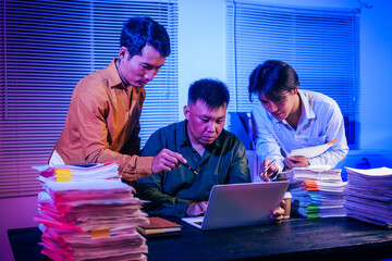Three men work overtime at night, stressed and overloaded with tasks. They are exhausted, checking...