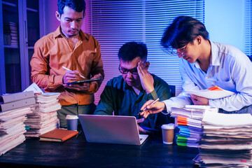 Three men work overtime at night, stressed and overloaded with tasks. They are exhausted, checking...