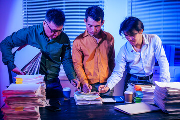 Three men work overtime at night, stressed and overloaded with tasks. They are exhausted, checking...