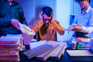Three men work overtime at night, stressed and overloaded with tasks. They are exhausted, checking...
