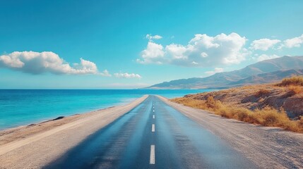 Fototapeta premium Long road stretching along the coast with sea views, bright blue skies, sunny landscape, endless journey, road trip destination, beach and mountains in distance