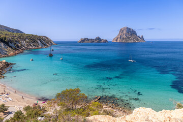 Vibrant scene of Cala Hort beach, Ibiza, featuring anchored boats and the stunning contrast of...