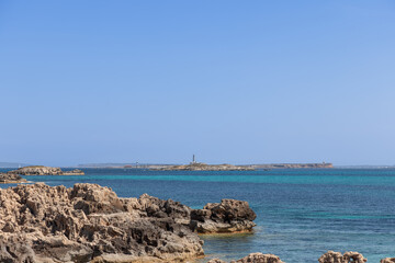 View from Ibiza rocky coastline towards the maritime islands of Formentera, featuring clear blue waters and distant lighthouses on the horizon