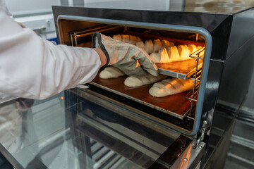 The baker puts the loaves of bread in the oven. Making bread in a mini bakery.