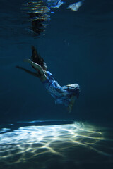Woman in dress swimming underwater in the pool