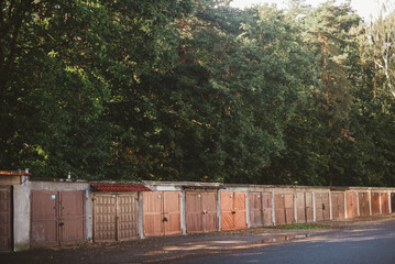 old garages with wooden doors against the background of green trees on a summer evening © Stepan