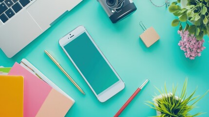 A Flat Lay of a Teal Desk with a Smartphone, Pens, Notebooks, and Plants