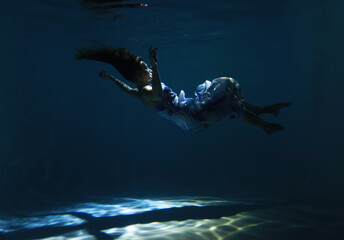 Beautiful woman in blue dress posing underwater as zero gravity in light beam