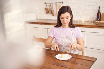Woman in polka dot apron enjoying macaron at cozy kitchen table with white brick background.