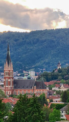 Tree branch framing distant view of majestic church Herz Jesu Kirche in Graz, Styria, Austria. Landmark against dramatic sky. Intricate architectural details, including pointed spire, ornate windows