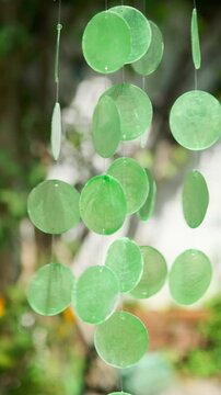An acoustics wind chime mobile with green capiz shells hanging in a garden and moving in the wind