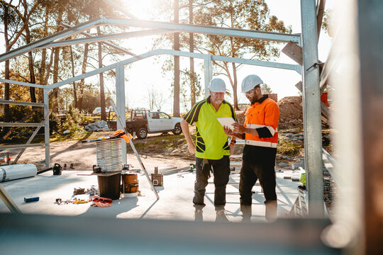 Focus on ute behind two construction site managers looking at digital blueprints
