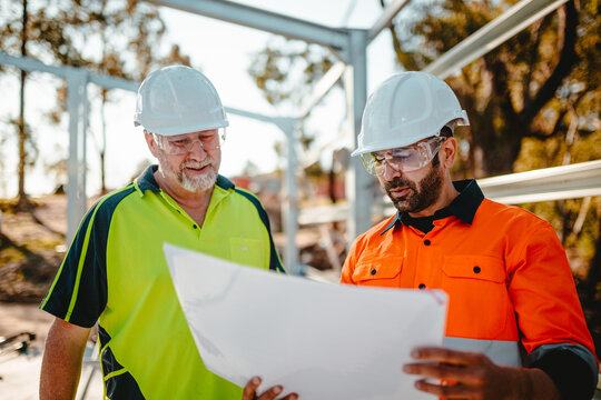 Builders in hardhats looking on blueprints at the construction site