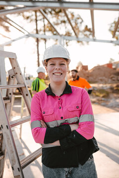 A young woman apprentice on construction site with arms crossed standing and smiling at the camera