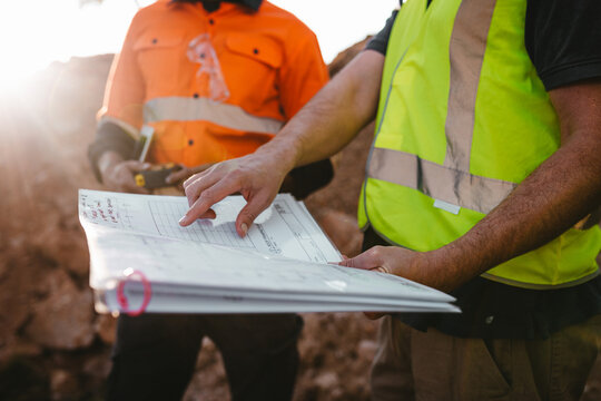 Builders pointing at the blueprint at the construction site